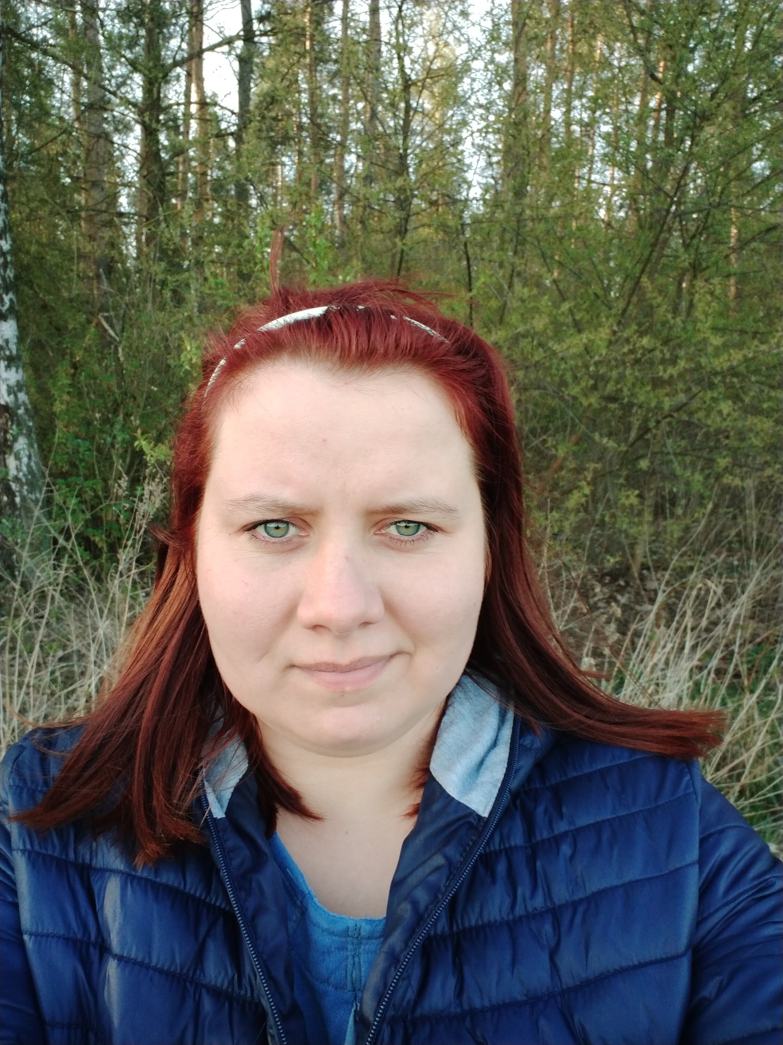 Portret kobiety z rudymi włosami i zielonymi oczami na tle lasu i krzewów w świetle popołudniowego słońca.