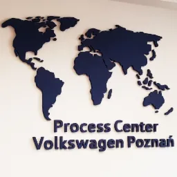 Granatowa, trójwymiarowa mapa świata i napis 'Process Center Volkswagen Poznań' przymocowane do białej ściany wewnątrz budynku, wykonane z tworzywa.