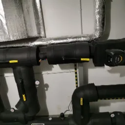 Izolowane rury grzewcze w piwnicy, widoczne zawory Ballomax, manometry oraz elektroniczna pompa obiegowa Evoplus Small z wyświetlaczem.