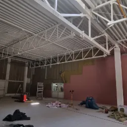 Wnętrze hali w trakcie ocieplania ścian wełną mineralną, widoczna konstrukcja dachu i świetlik