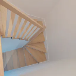 Widok z góry na drewniane schody spiralne z jasnego drewna z białymi balustradami w jasnym wnętrzu.