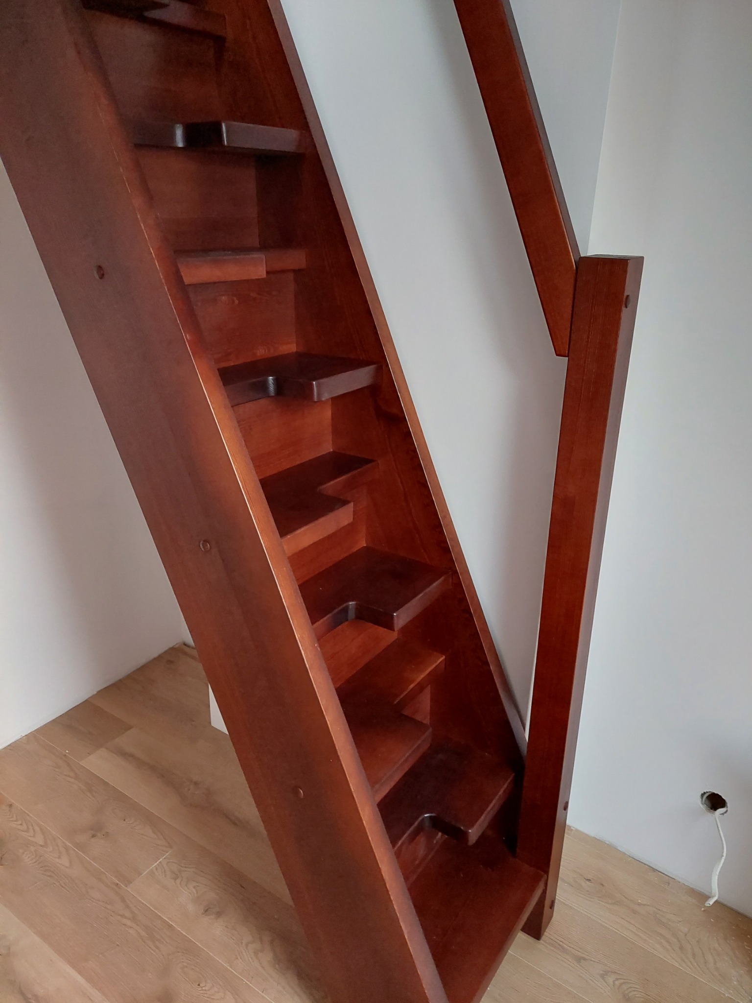 Kompaktowe, ciemne schody drewniane z poręczą, zamontowane w domu w Brodnicy Górnej, widoczne z dołu pod kątem.