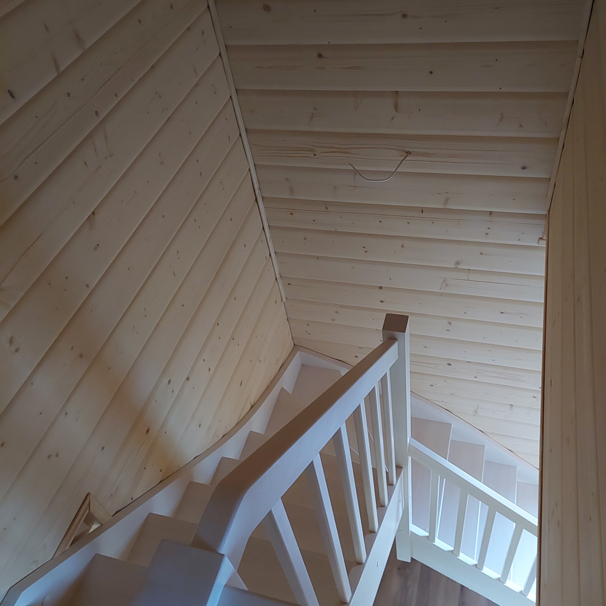 Białe schody z drewnianą balustradą w jasnym wnętrzu wykończonym boazerią.