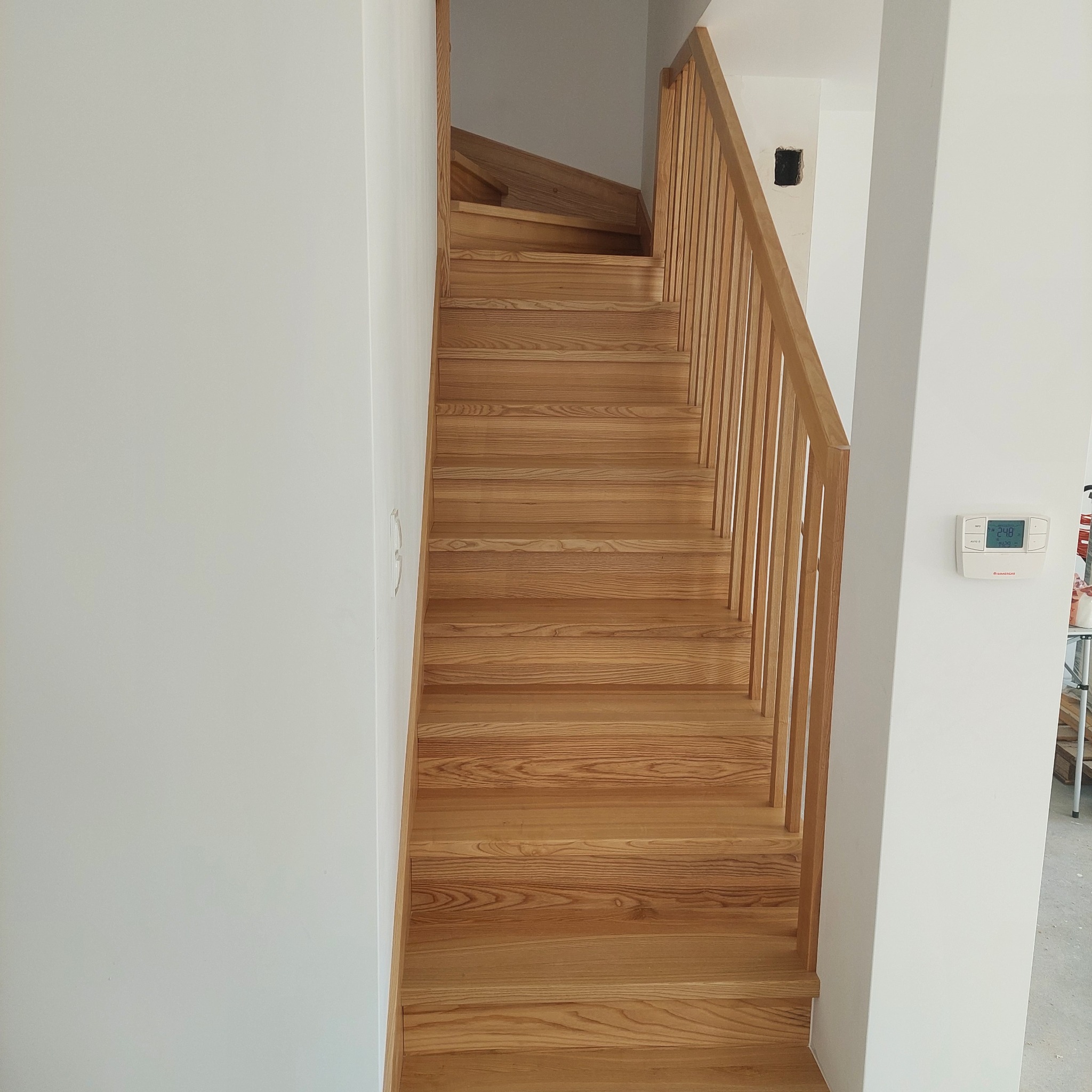 Naturalne, jasne drewniane schody z prostymi balustradami w minimalistycznym, białym wnętrzu, widok z dołu do góry.