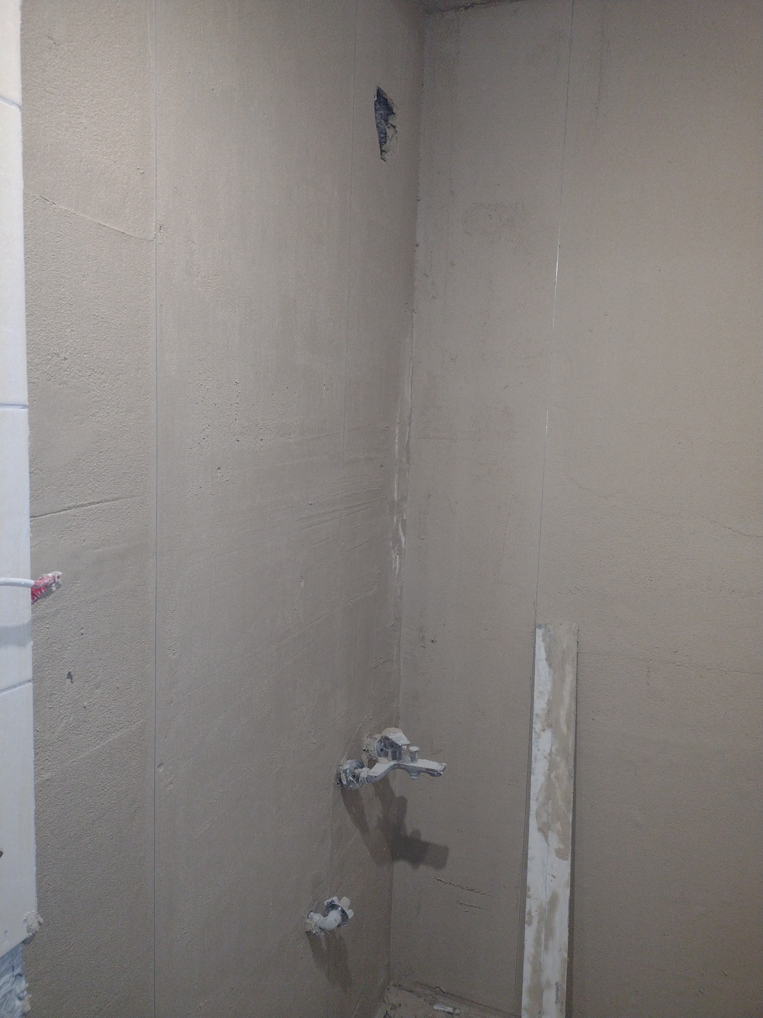 Ściany w łazience w trakcie wyrównywania i przygotowywania pod płytki, widoczne rury instalacji wodnej i pionowa listwa wyrównująca.