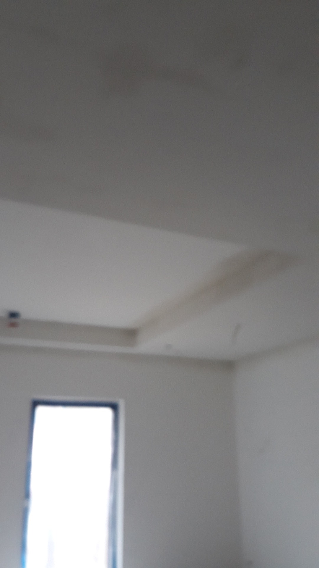 Niedokończone wnętrze z oknem, widoczne ślady po pracach na suficie, brak wykończenia ścian.