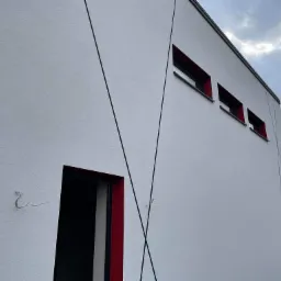 Nowoczesna elewacja budynku w Grudziądzu z białym tynkiem strukturalnym, czerwonymi obramowaniami okien i drzwi oraz dekoracyjnymi czarnymi liniami na ścianie.