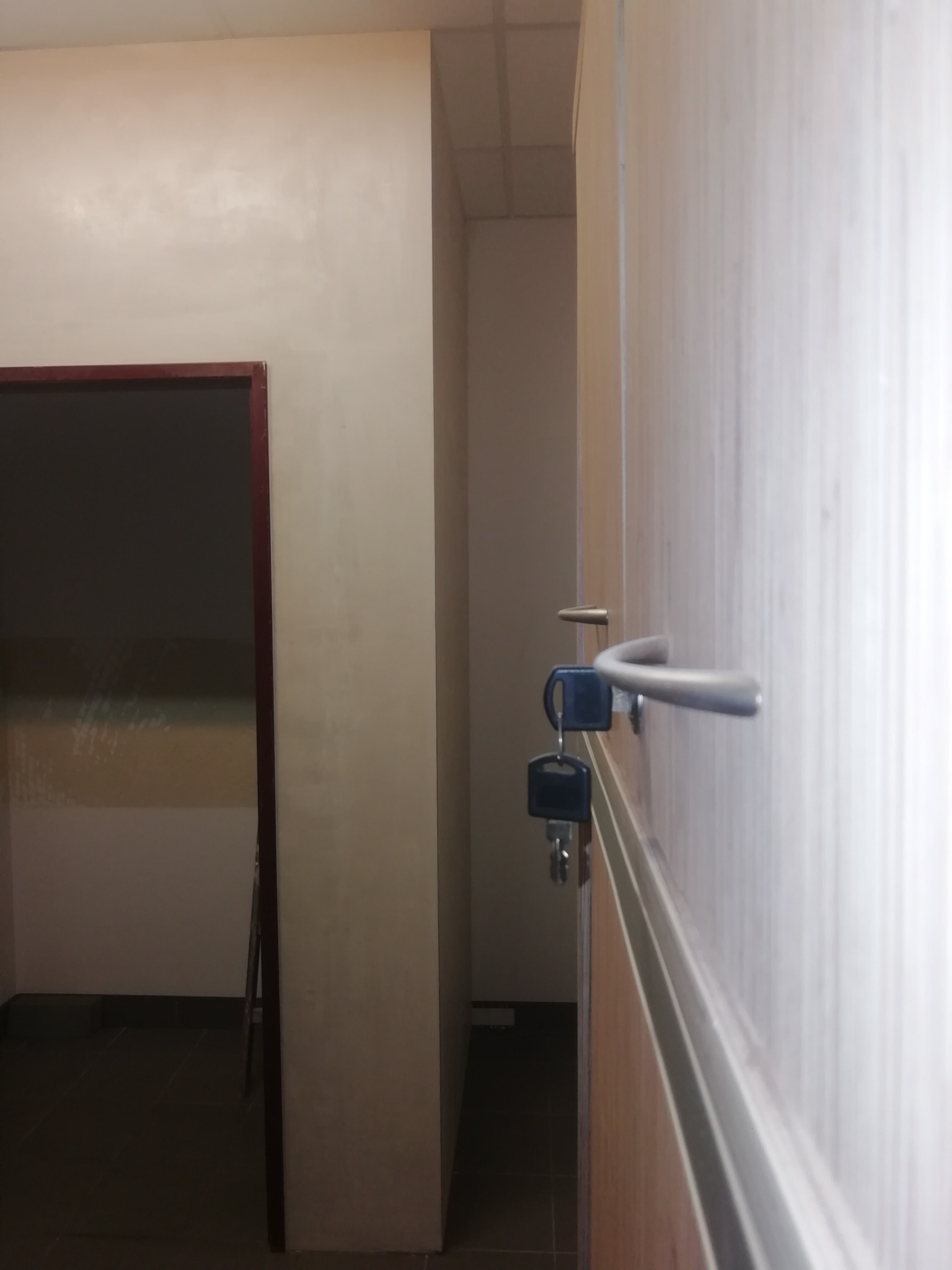 Klucze w zamku drzwi wewnętrznych, widok z perspektywy korytarza, ściana pomalowana na jasny kolor w tle.