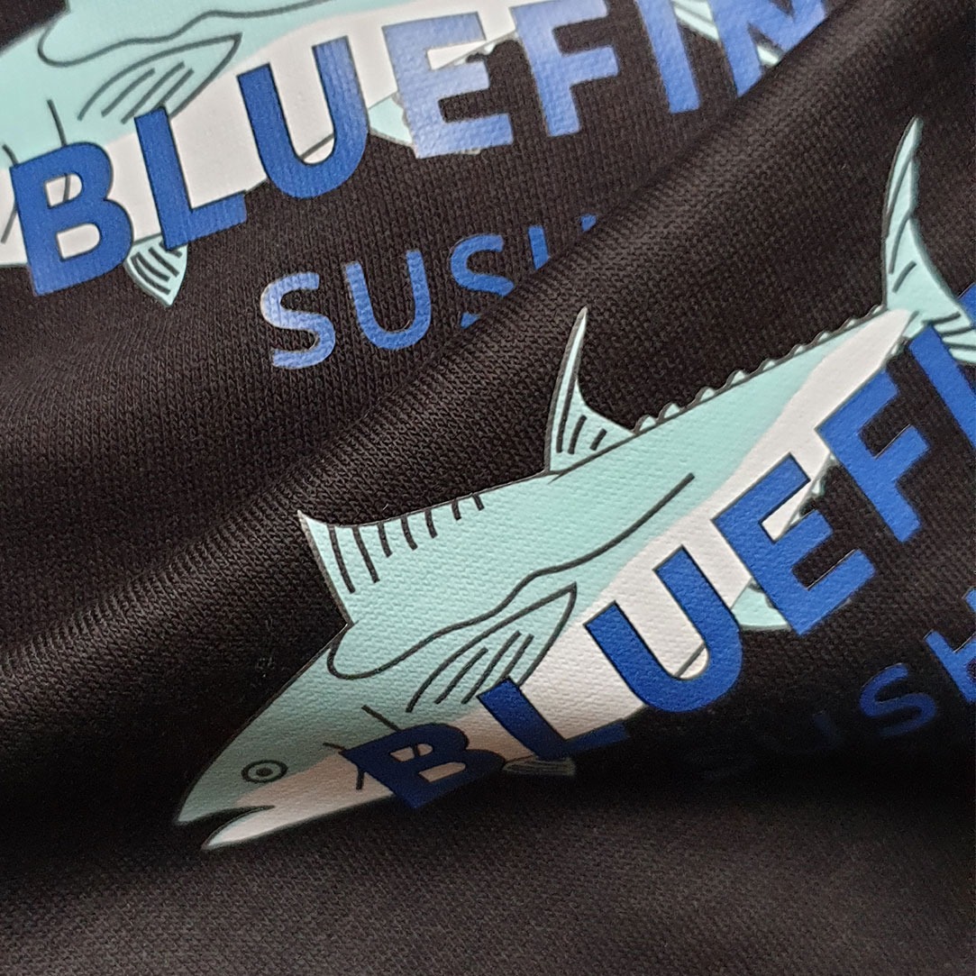Czarna koszulka z nadrukiem grafiki tuńczyka i napisu 'BLUEFIN SUSHI' w odcieniach błękitu i bieli, widoczna faktura materiału.