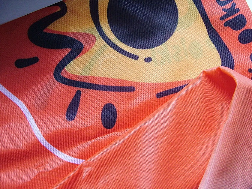 Pomarańczowa tkanina z nadrukowanym dużym, kreskówkowym wzorem w odcieniach żółci i czerni, złożona w fałdy.