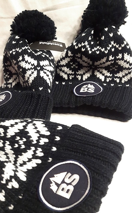 Trzy czarne wełniane czapki zimowe z białym wzorem w płatki śniegu i naszytym okrągłym logo 'BS', jedna z metką