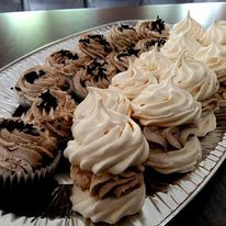 Srebrna taca z rzędami babeczek: czekoladowych z posypką i bezowych z kremem, ustawionych naprzemiennie.