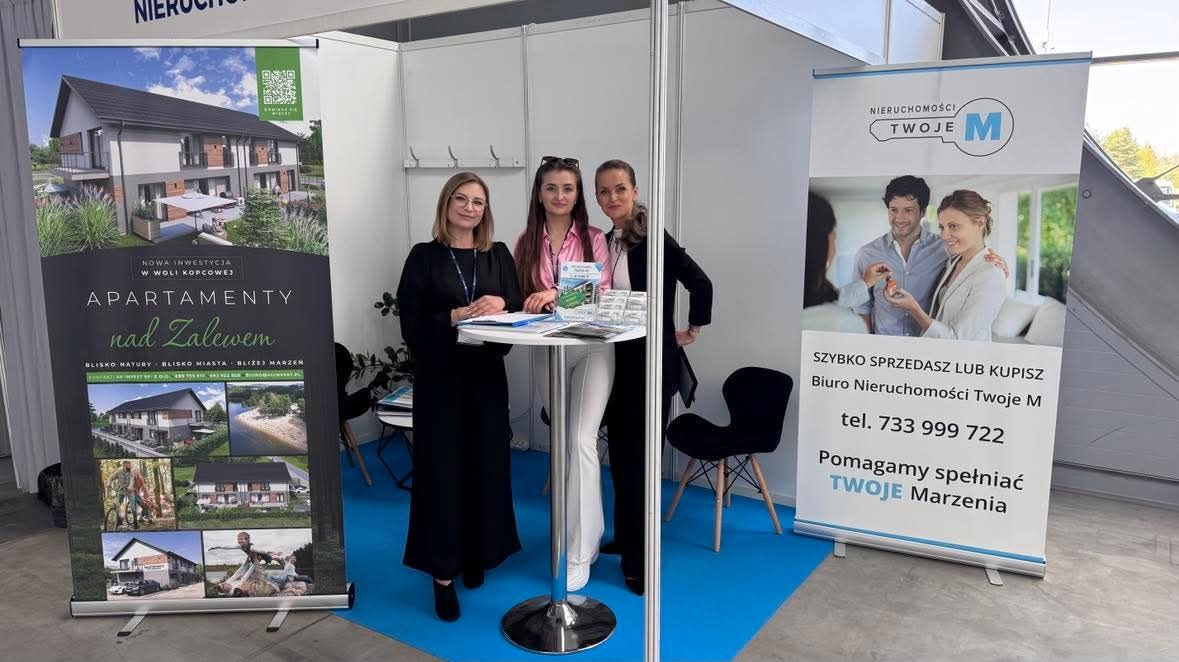 Stoisko targowe biura nieruchomości z trzema kobietami, roll-upy z ofertą apartamentów i hasłem 'Szybko sprzedasz lub kupisz'.