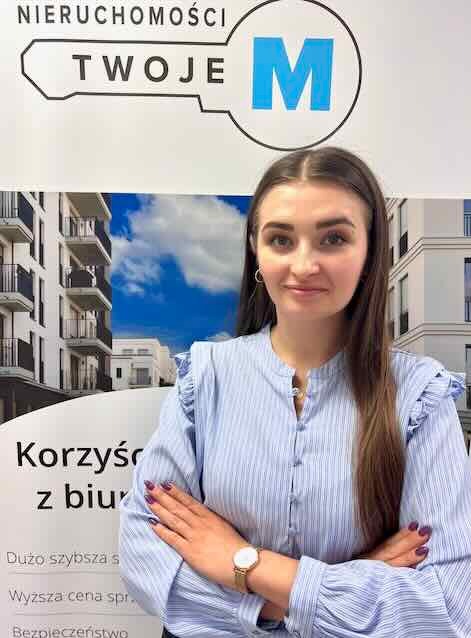 Pracownica biura nieruchomości na tle grafiki z budynkiem mieszkalnym i logo firmy. Kobieta w bluzce w paski, z zegarkiem na ręku, skrzyżowanymi rękoma i z uśmiechem.