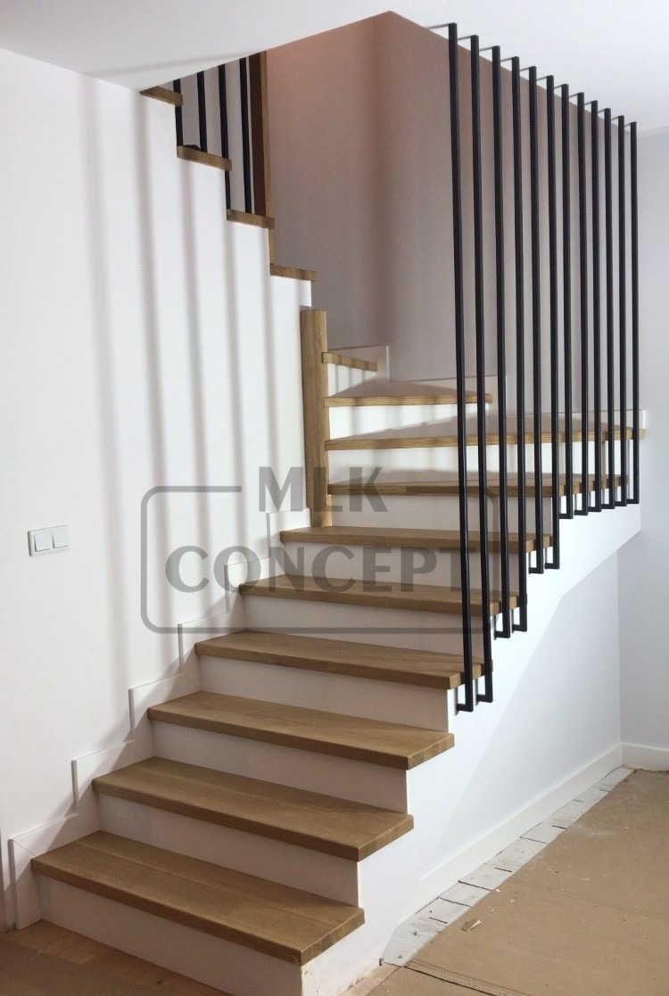 Jasne drewniane schody z czarnymi, pionowymi balustradami w nowoczesnym wnętrzu, widok z dołu na pierwsze stopnie.