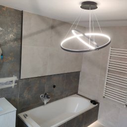 SajgonBUD usługi remontowo-budowlane - Nowoczesna łazienka w trakcie wykańczania: biała wanna, grzejnik drabinkowy, okrągłe lustro i designerska lampa. Widoczne zabezpieczenia na elementach.