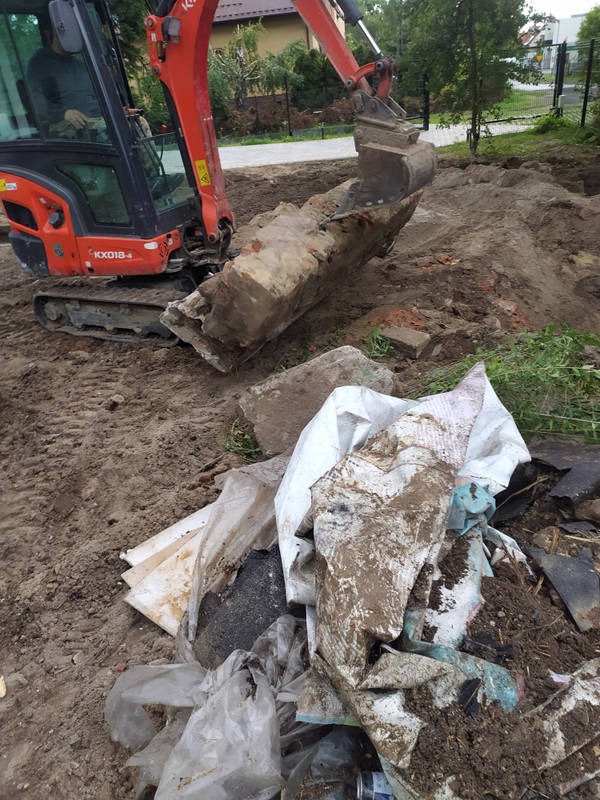 Mini koparka Kubota podnosi gruz i odpady budowlane na placu budowy. Widoczne ślady pracy w ziemi i nagromadzony gruz. Etap porządkowania terenu.