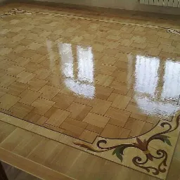 Wypolerowana, błyszcząca podłoga z parkietu ułożonego w kwadraty, z dekoracyjnym ornamentem w narożnikach, odbijająca światło okien.