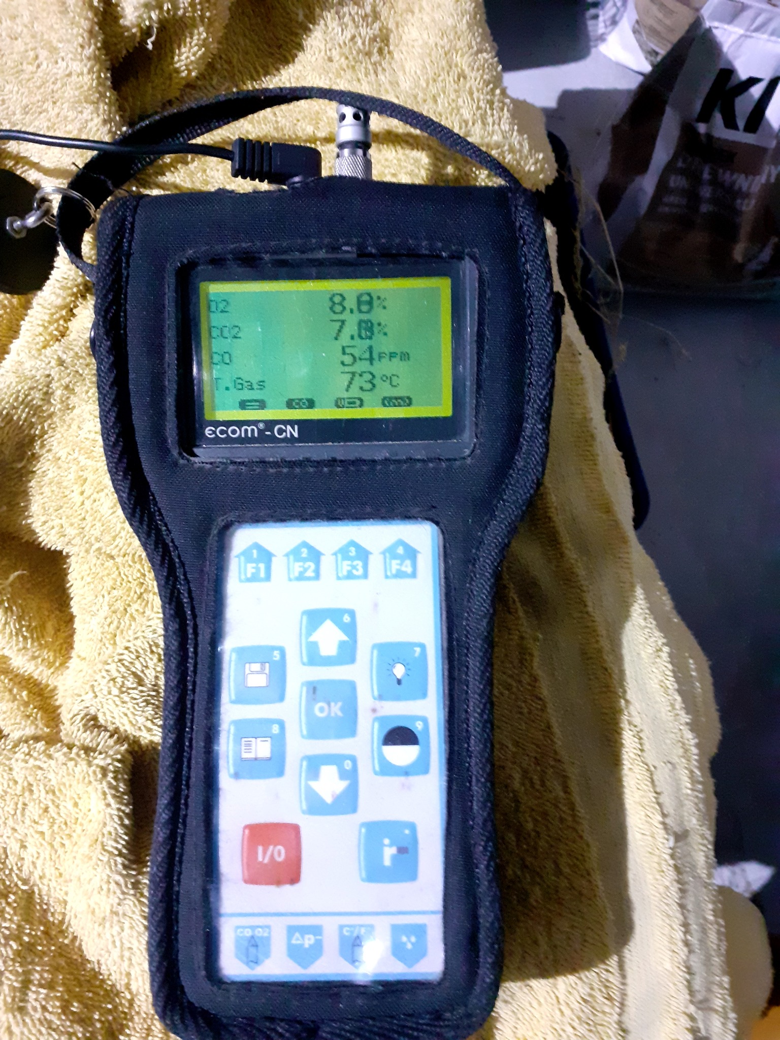 Analizator spalin Ecom-CN wyświetlający pomiary O2, CO2, CO i temperatury gazu, leżący na żółtej ściereczce.