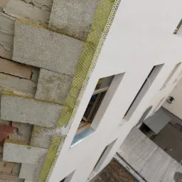 Ocieplanie elewacji budynku z widoczną warstwą izolacji termicznej z wełny mineralnej, siatką wzmacniającą i częściowo nałożonym tynkiem.