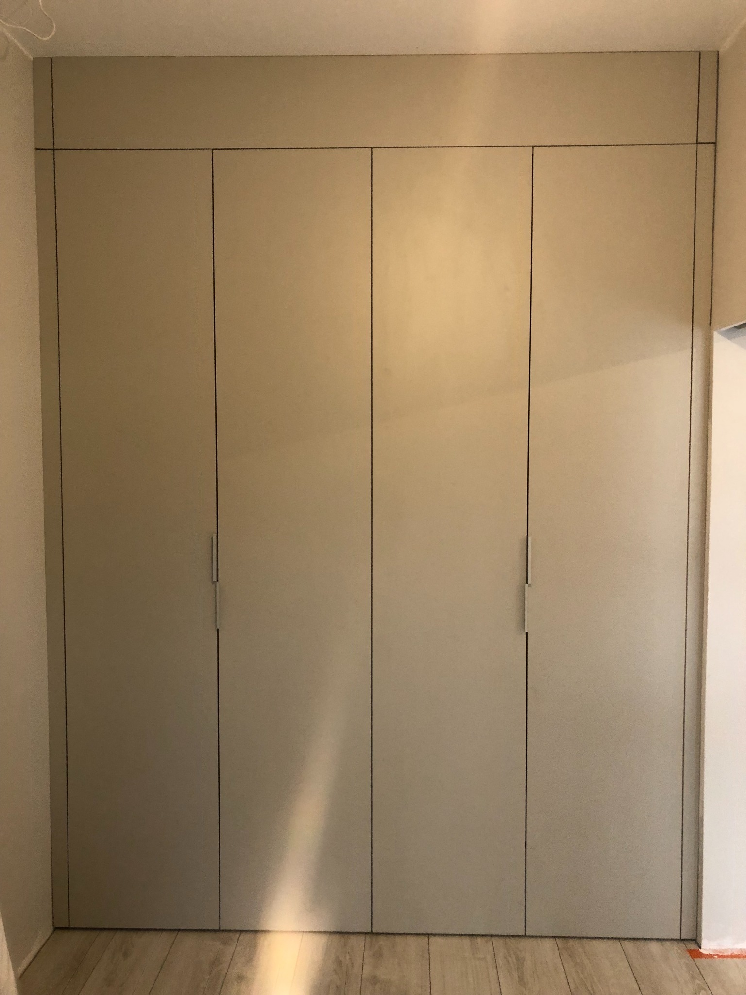 Czterodrzwiowa, beżowa szafa wnękowa z minimalistycznymi uchwytami, dopasowana do skosu sufitu w Groblicach.