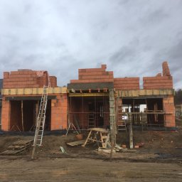 B.R.T- BP Sp. z o.o. - Wznoszenie ścian parterowego domu z czerwonej cegły ceramicznej, widoczne szalunki i rusztowania na tle pochmurnego nieba.