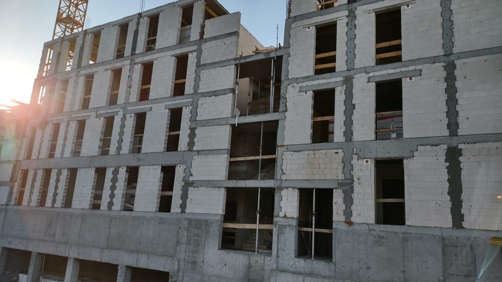 Wznoszenie wielopiętrowego budynku z betonu komórkowego, widoczne surowe ściany z otworami okiennymi i betonowe elementy konstrukcyjne, żuraw budowlany w tle.