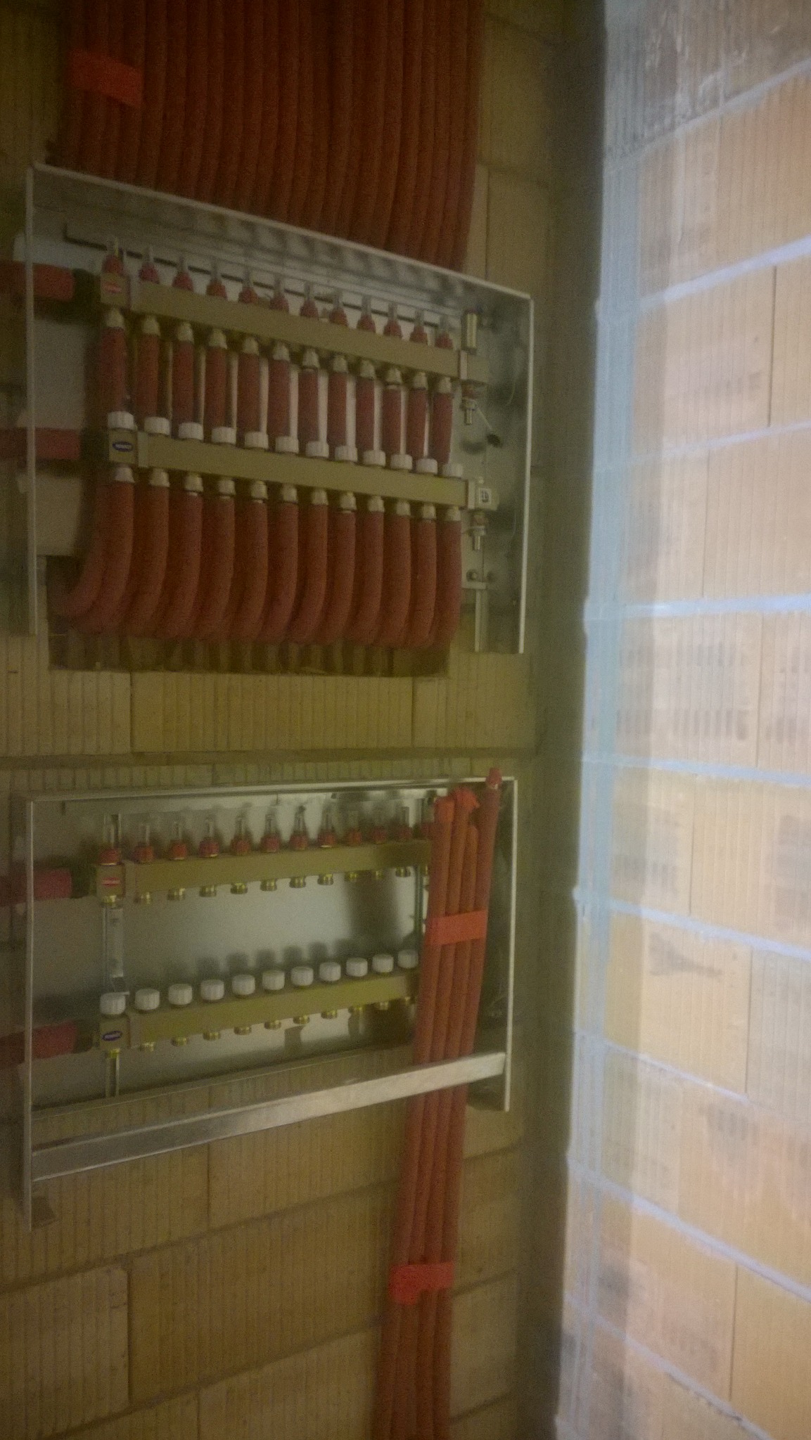 Rozdzielacze ogrzewania podłogowego w metalowych szafkach, zamontowane na ścianie z pustaków ceramicznych.