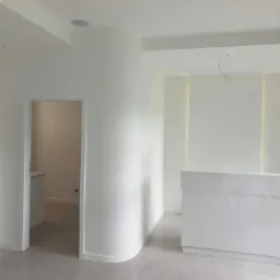 Nowoczesne, minimalistyczne wnętrze w Białystoku z białą, zaokrągloną ścianą, szarą podłogą i recepcją w połysku, widok na sąsiednie pomieszczenie.