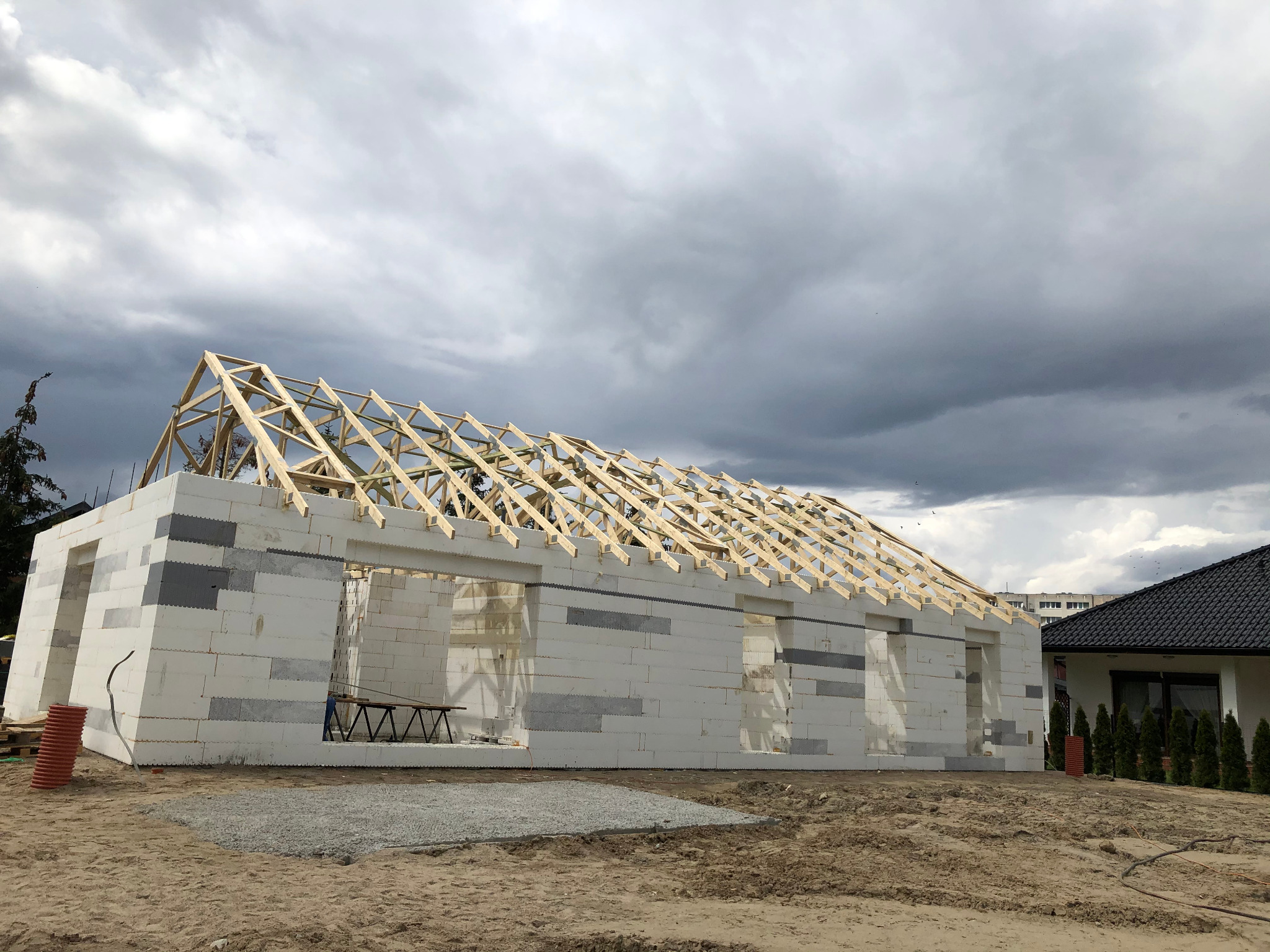 Budowa domu w systemie szalunku traconego z drewnianą konstrukcją dachu na tle pochmurnego nieba.