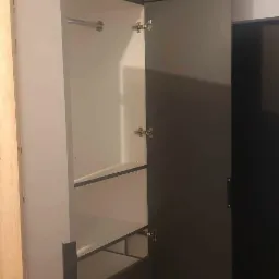 Wysoka szafa z otwartymi drzwiami i szufladami, widoczne półki i drążek na ubrania, połączenie białych i grafitowych elementów.