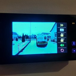 Electro Zych - Ekran wideodomofonu wyświetlający obraz z kamery: widok na ulicę i zaparkowany samochód dostawczy z logo firmy.