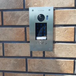 Panel wideodomofonu Vidos z klawiaturą numeryczną, zamontowany na ceglanym murze zewnętrznym.