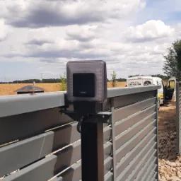 Zamontowany napęd FAAC na szarej, metalowej bramie posesji z widocznym w tle polem i firmowym samochodem serwisowym.