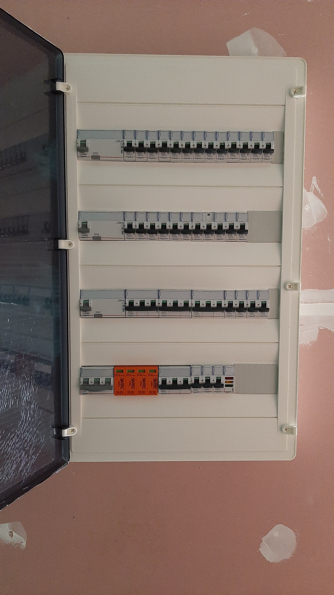 Otwarta skrzynka rozdzielcza z bezpiecznikami i ogranicznikiem przepięć na ścianie w trakcie wykańczania.