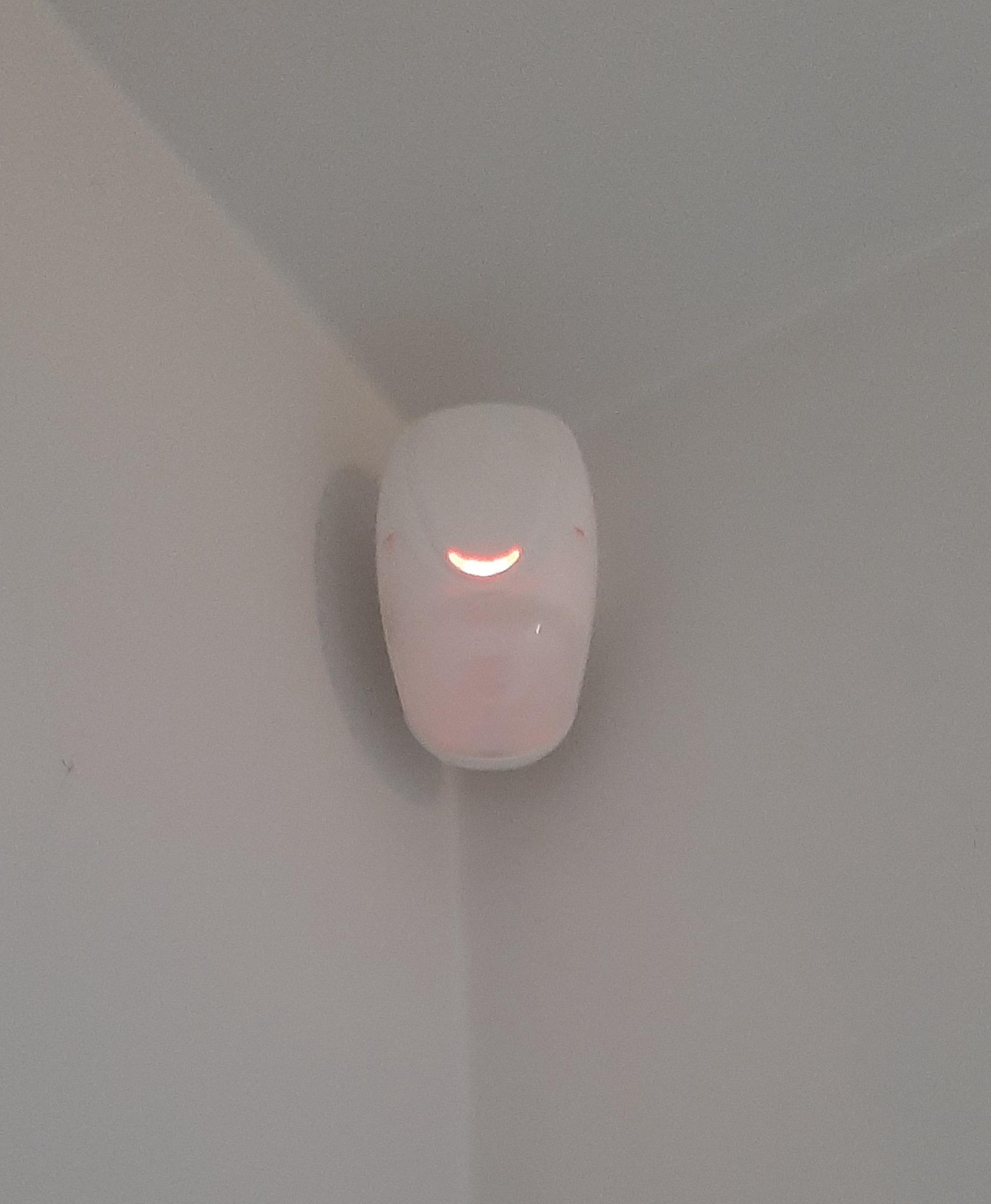 Biały czujnik alarmowy z czerwoną diodą zamontowany w rogu pomieszczenia o jasnych ścianach.