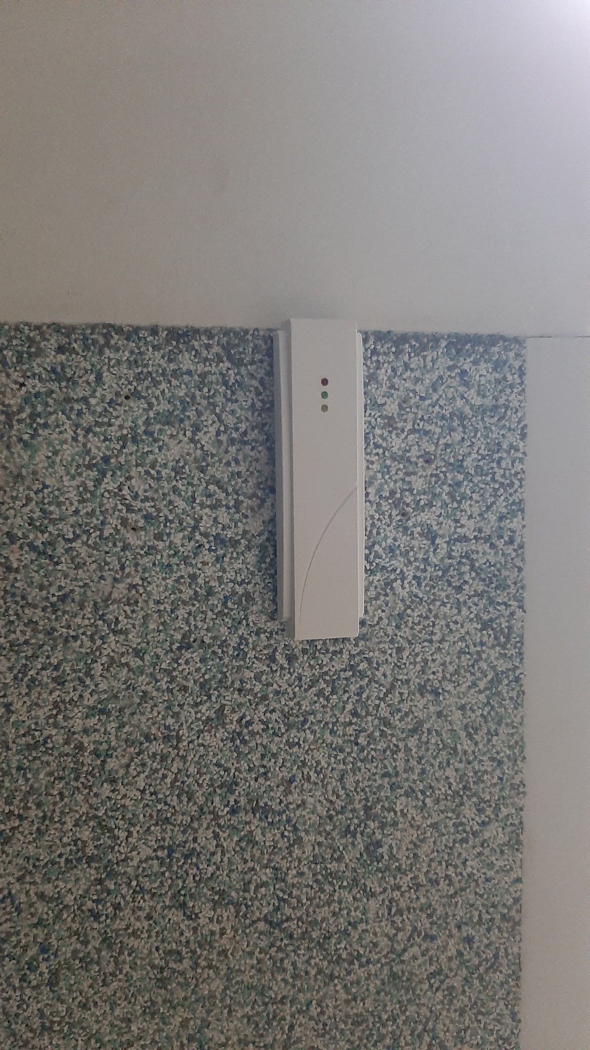 Biały panel sterowania z trzema diodami LED, zamontowany na ścianie o fakturze drobnego kamyczka.