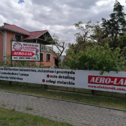 Budynek firmy blacharsko-lakierniczej z banerem reklamowym oferowanych usług, w tym auto detailing i usługi stolarskie.