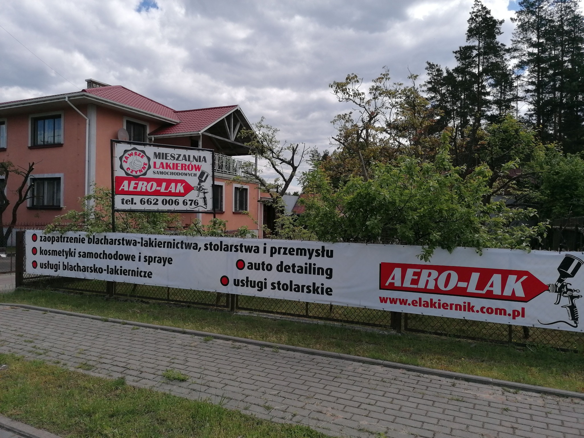 Budynek firmy blacharsko-lakierniczej z banerem reklamowym oferowanych usług, w tym auto detailing i usługi stolarskie.