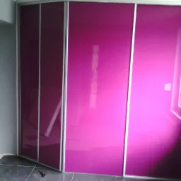 Fioletowa szafa wnękowa z przesuwnymi drzwiami i srebrnymi ramami, częściowo otwarta, na tle szarej ściany i ciemnych płytek podłogowych.