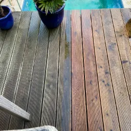 Częściowo wyczyszczony drewniany taras przy basenie, widoczna różnica w kolorze drewna, donice z roślinami i fragment mebli ogrodowych.