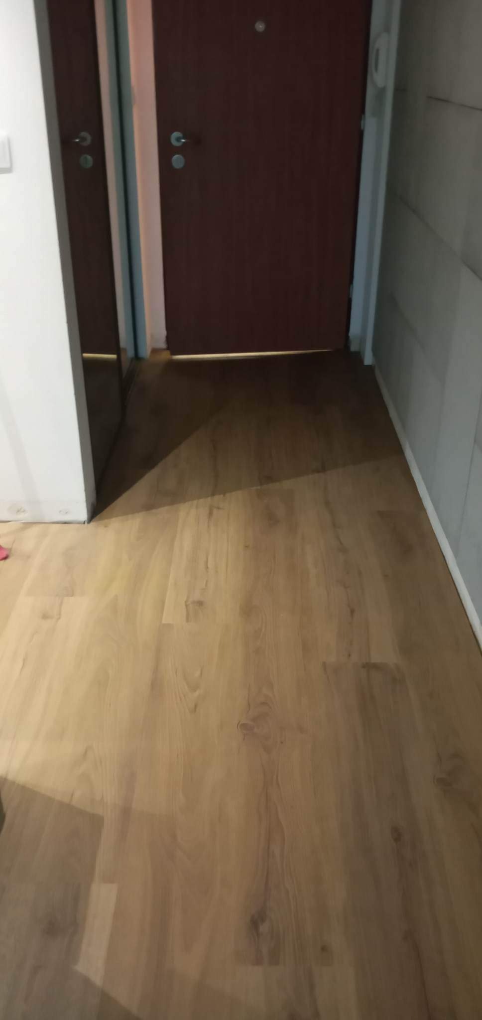 Nowo położony parkiet o jasnym odcieniu drewna, widoczny fragment brązowych drzwi i szara ściana w tle.