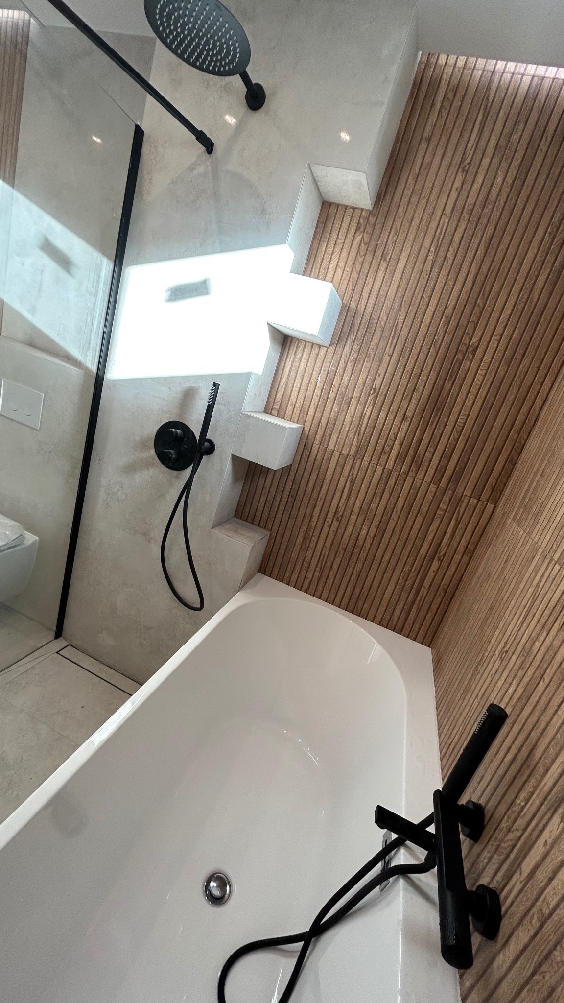 Nowoczesna łazienka z białą wanną, czarną armaturą i ścianą wykończoną drewnianymi panelami w pionowe prążki, widok z góry.