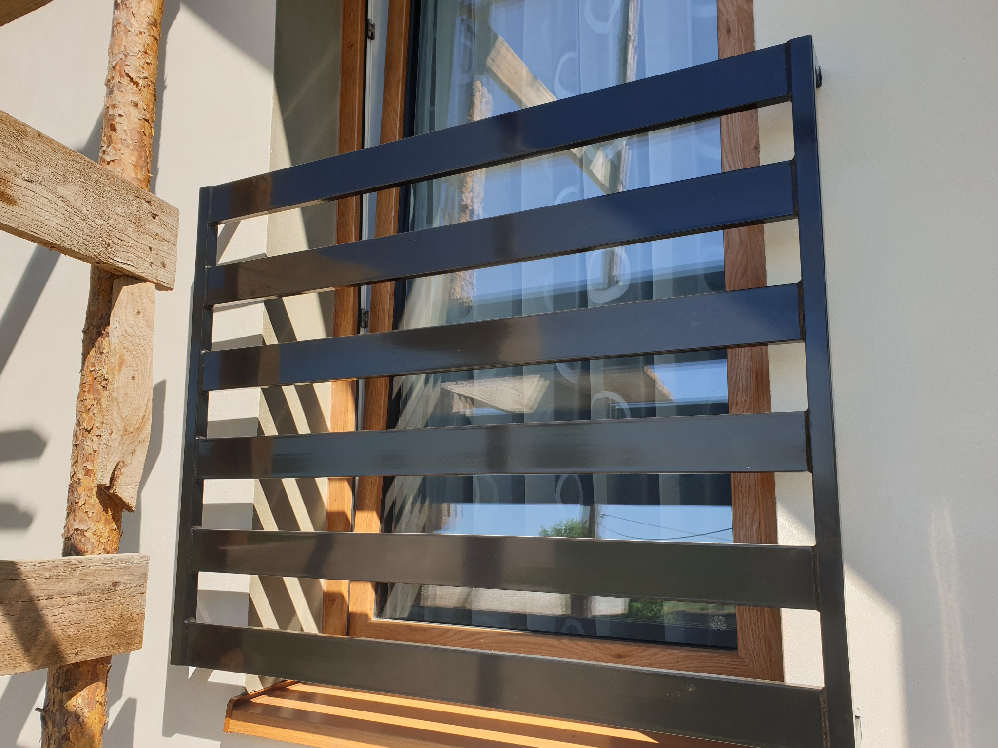 Czarna, pozioma, metalowa krata okienna zamontowana na elewacji budynku z widocznymi rusztowaniami drewnianymi z boku.