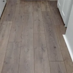 Ułożone panele podłogowe w odcieniach szarości w pomieszczeniu z białym grzejnikiem i listwami przypodłogowymi w Olkuszu.