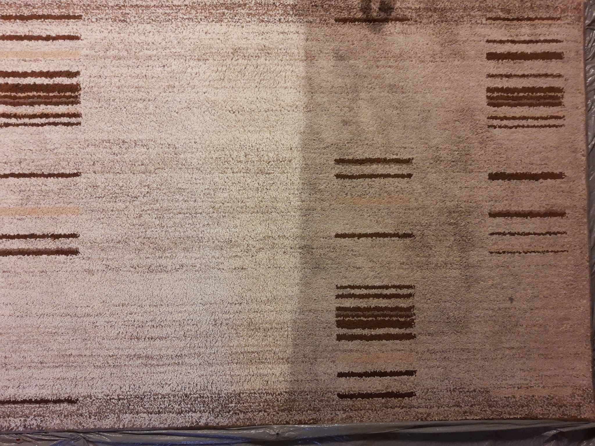 Dywan w odcieniach beżu i brązu, z widoczną różnicą czystości po lewej stronie, ukazując efekt przed i po zabiegu czyszczenia, z wzorem w paski.