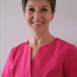 Portret uśmiechniętej kobiety w różowej bluzce na jasnym tle, prawdopodobnie specjalistka z branży beauty lub medycyny naturalnej.