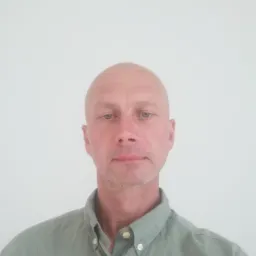 Portret mężczyzny o łysiejącej głowie, w zielonej koszuli z kołnierzykiem, na białym tle.