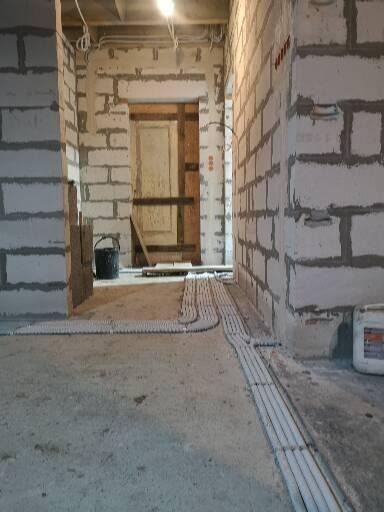 Wewnętrzne kable elektryczne ułożone w bruzdach w podłodze surowego budynku z bloków, widoczne puszki instalacyjne w ścianach.