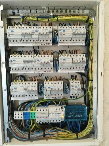 Otwarta skrzynka elektryczna z zainstalowanymi bezpiecznikami, przewodami różnej grubości i koloru, oraz elementami montażowymi na szynie DIN.